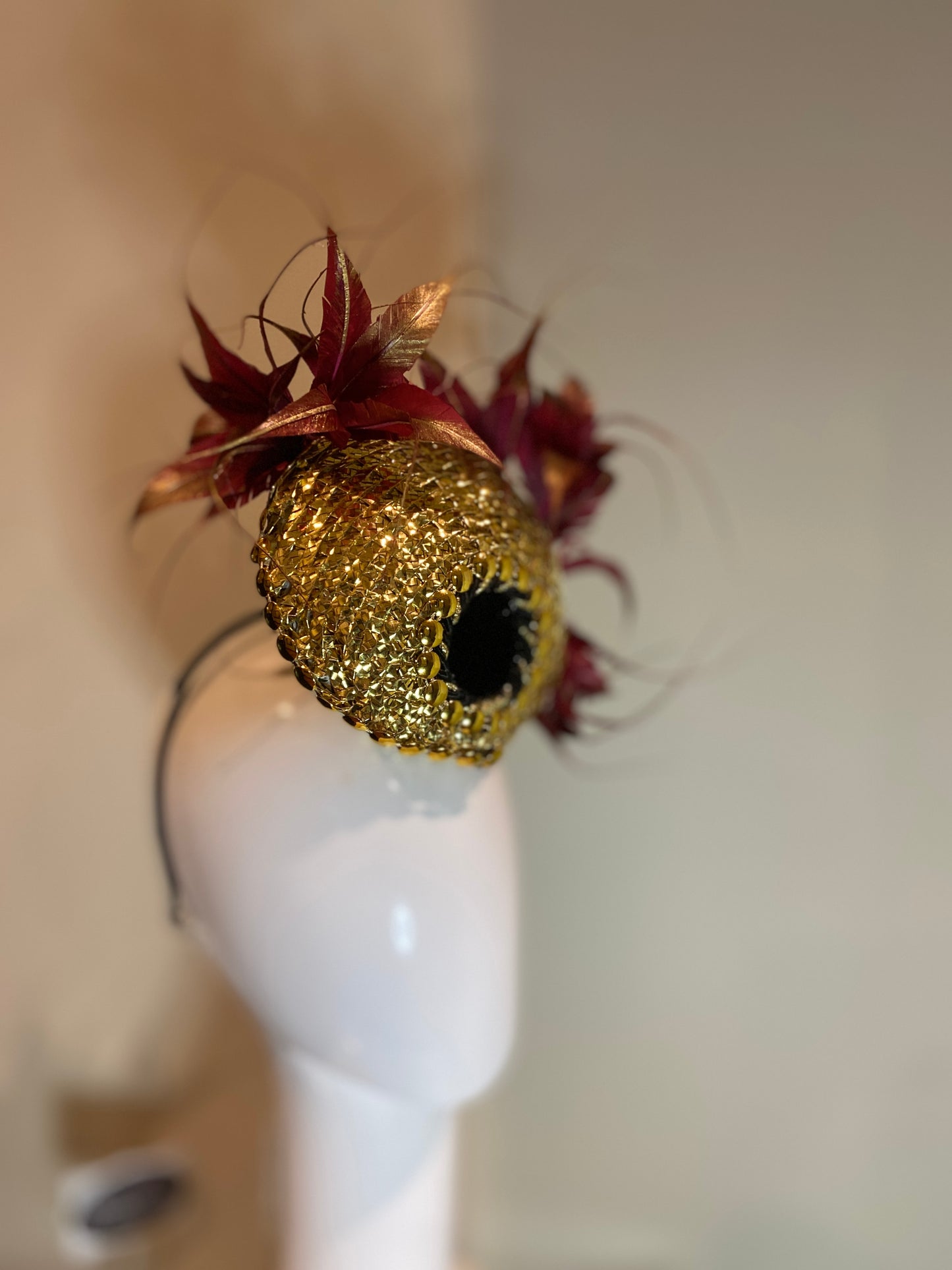 Hand woven gold disc with feather plume in maroon