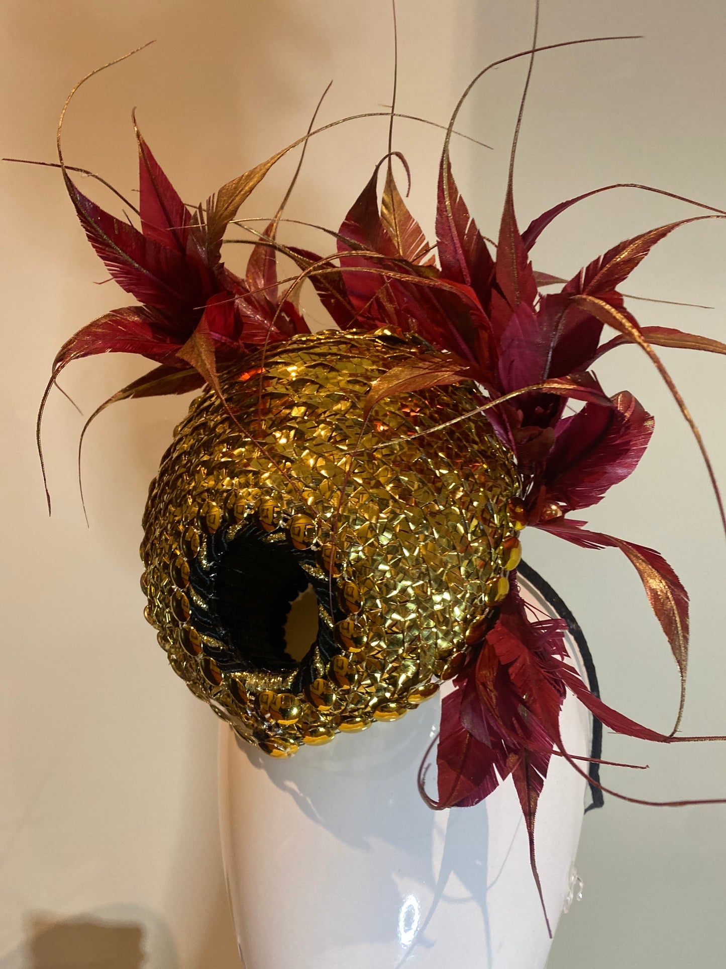 Hand woven gold disc with feather plume in maroon